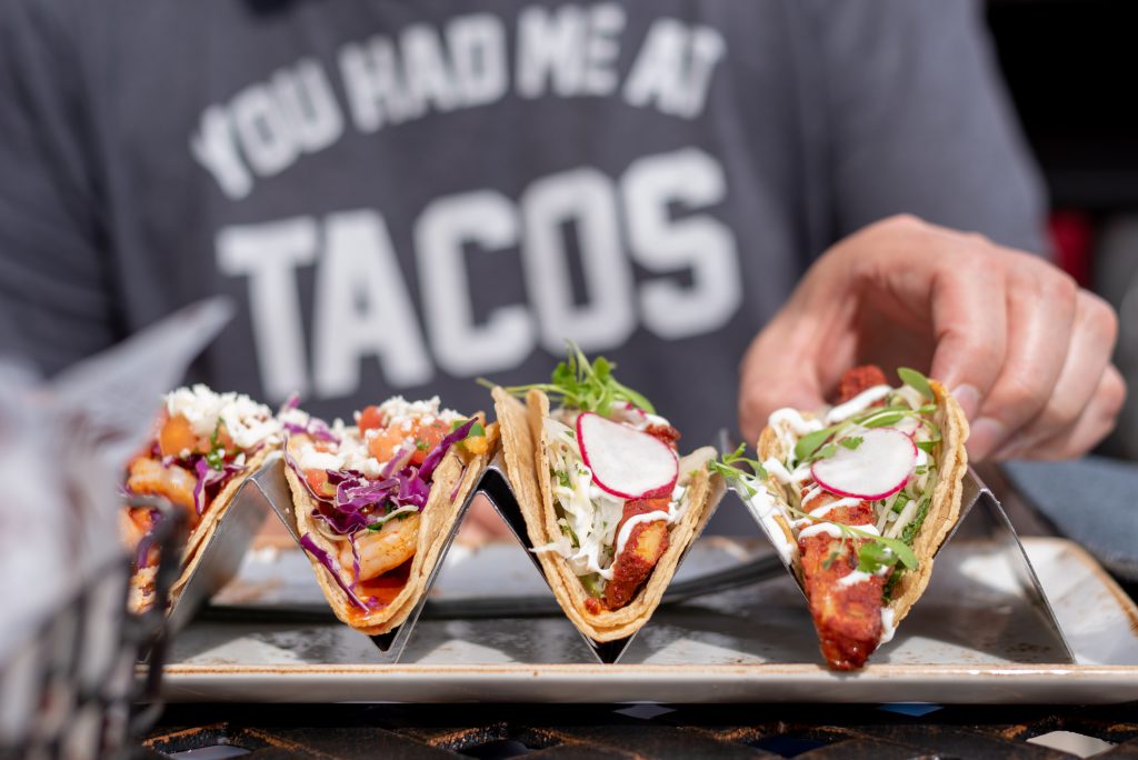 closeup of man eating tacos in summer with a shirt that says you had me at tacos in the background