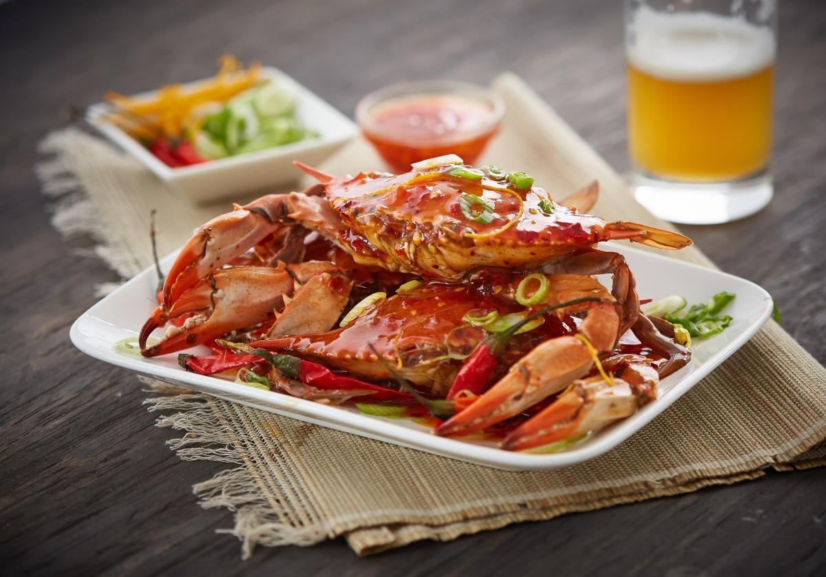 steamed blue crab dinner with onion garnish, beer in background and relish on a tan placemat and brown table top