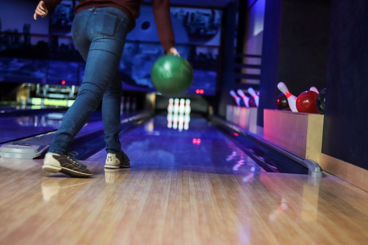 bowling lane with someone in jeans and bowling shoes with green bowling ball getting ready to throw at the pins at the end of the lane