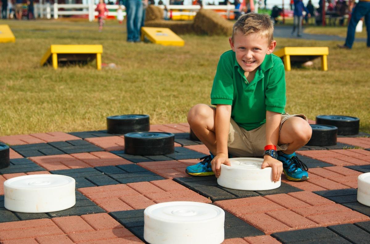 lever young boy playing a life size checkers game outside on a sunny day.
