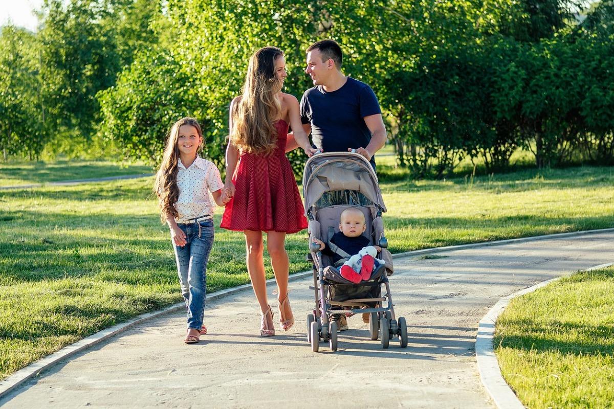 Happy big family walks in the summer park. beautiful long-haired woman her husband with her daughter and son in a stroller rest on the nature